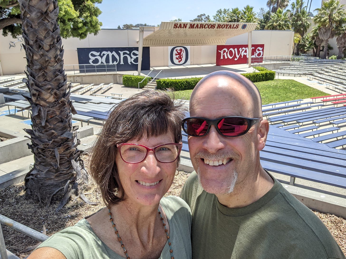 Two people smiling at the camera with an outdoor stadium behind them