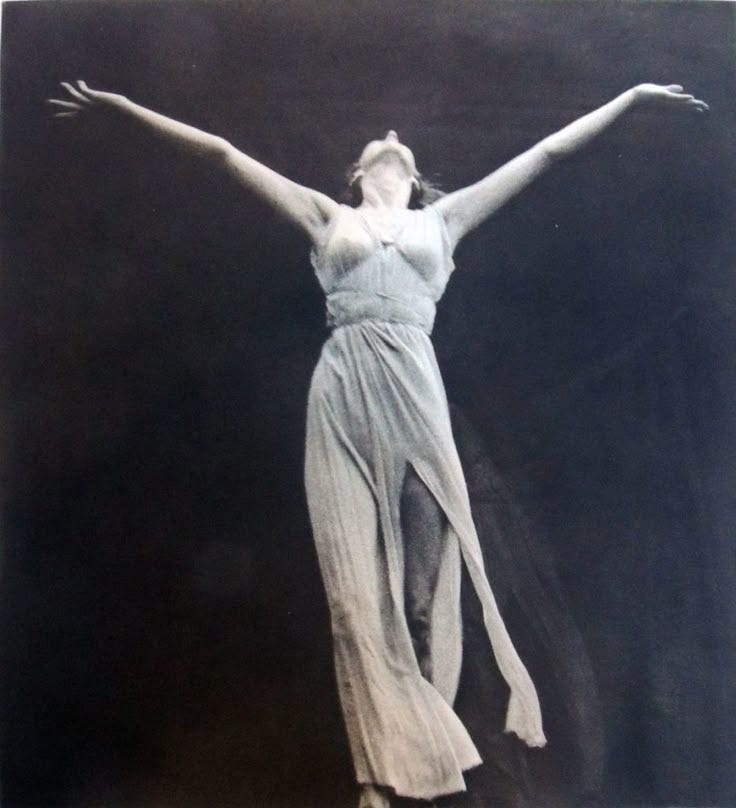 Black-and-white image of Isadora Duncan, arms outstretched, head tilted back, mid-motion. Her face is unseen. A moment of fierce, feminine freedom and surrender.