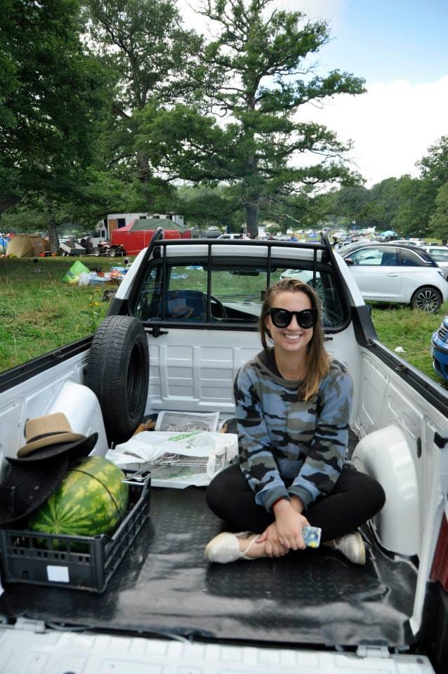 Cassandra sitting in the back of a white pick up truck next to a black milk crate with a large watermelon inside it.