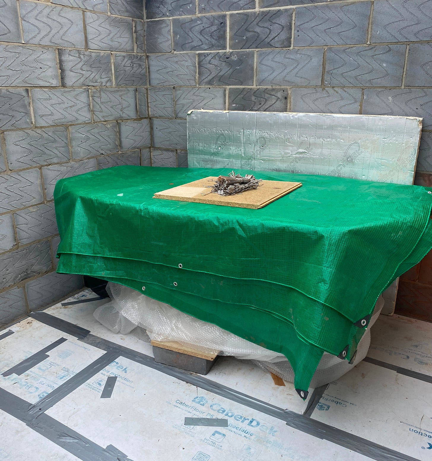 bath wrapped in bubble warp and a green taupaulin positioned against the block work inside the extension