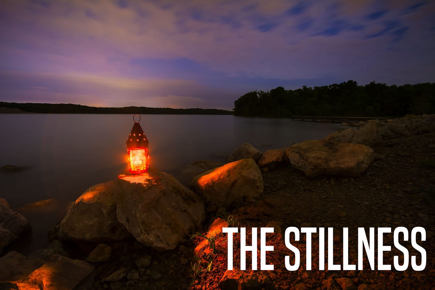 A photo of a rocky coast at sunset with a lone torch illuminating the foreground. The text "The Stillness" written in white.