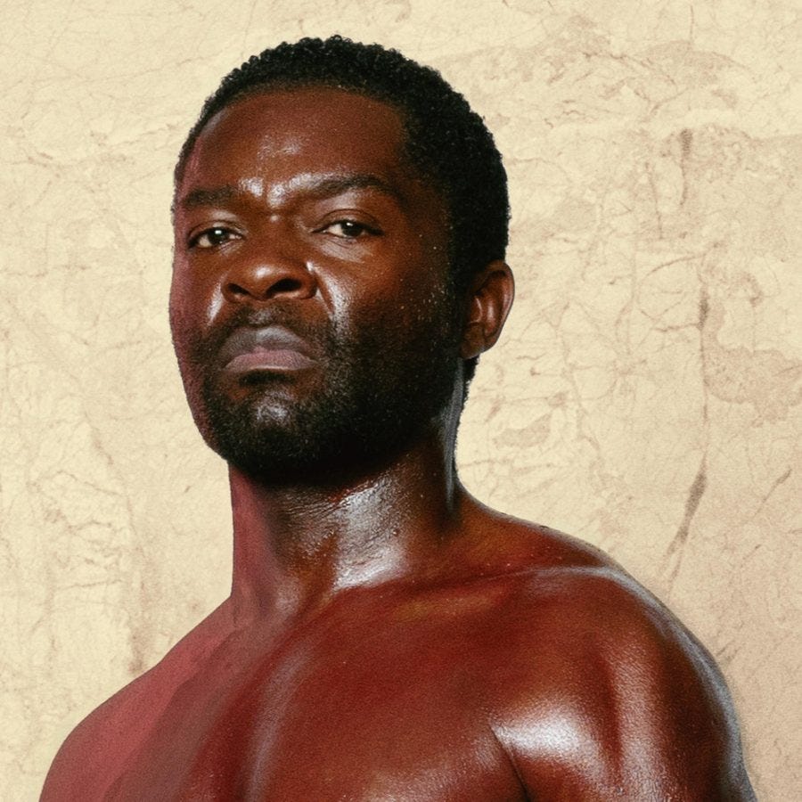 A photo of the head and shoulders of a man (David Oyelowo), wearing nothing. He stands against a roughly rendered, light coloured wall.