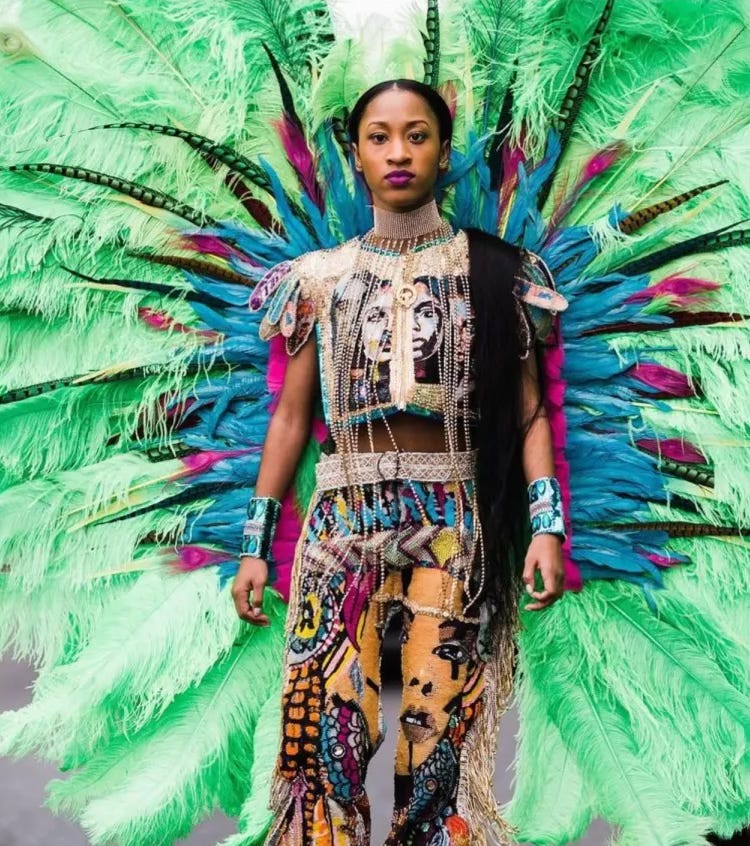 A woman in an elaborate carnival costume stands confidently, wearing a beaded outfit with artistic face prints, vibrant jewelry, and a massive green and blue feathered headdress.