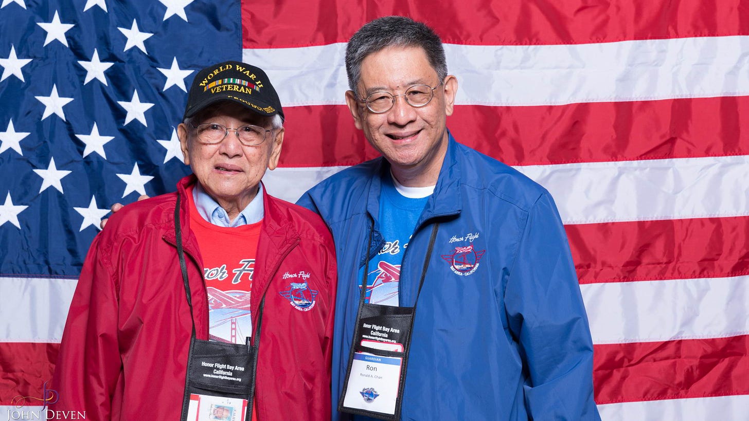 Alfred and Ron Chan on their Honor Flight in front of a wall-spanning flag.