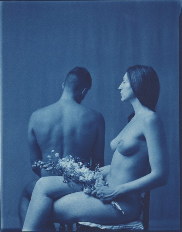 Photo cyanotype d'un homme et d'une femme nus. L'homme tourne le dos et la femme est vue de côté, avec des fleurs dans les mains.