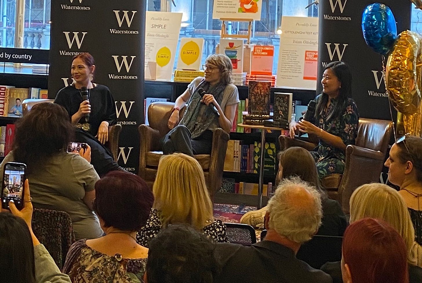 A photo of Sooz at an event with Elizabeth May and Daphne Tong, talking at the front of a packed room in Waterstones.