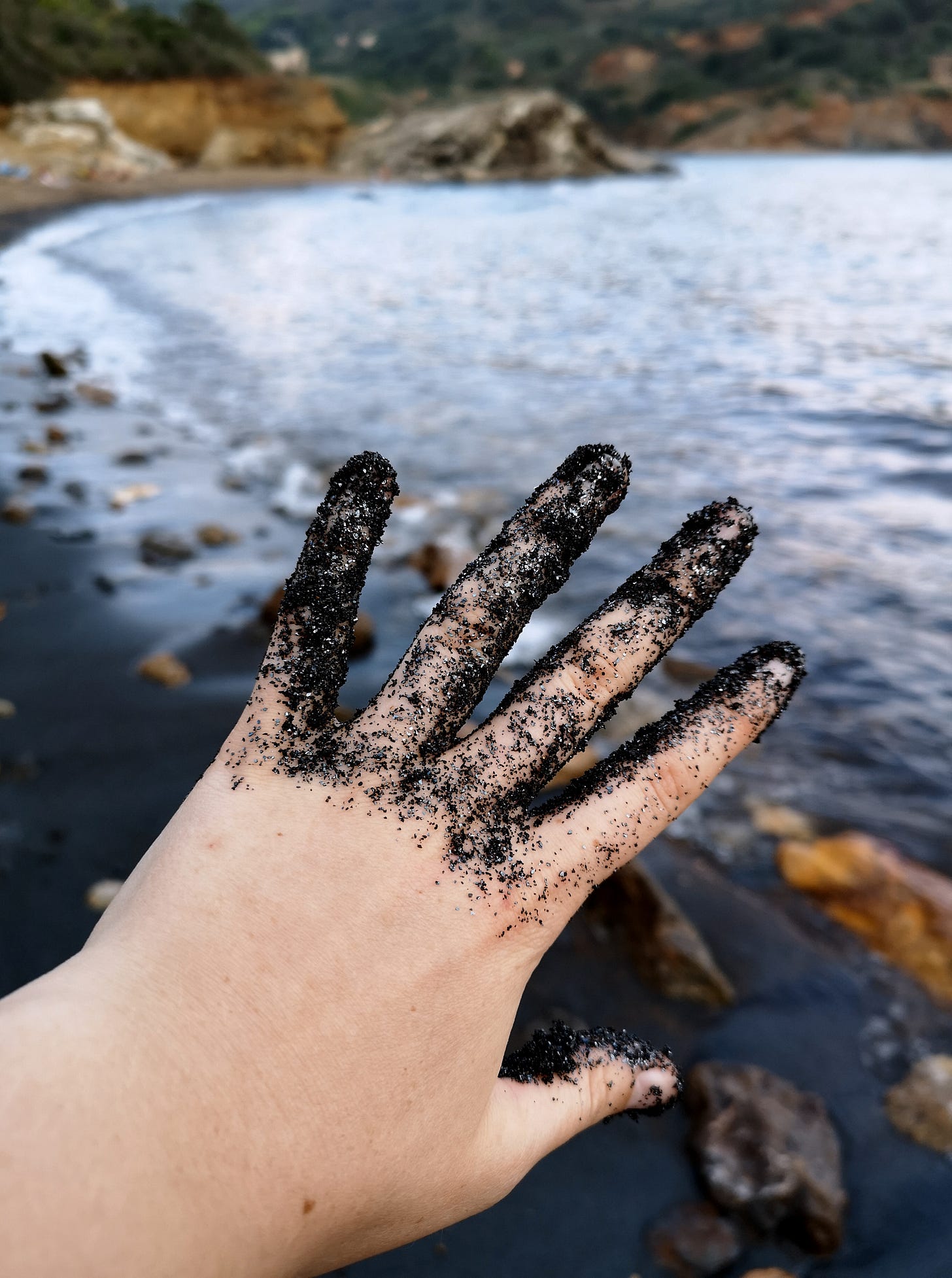 Black sand sparkles. White hand, black beach background, hematite sand covering hand