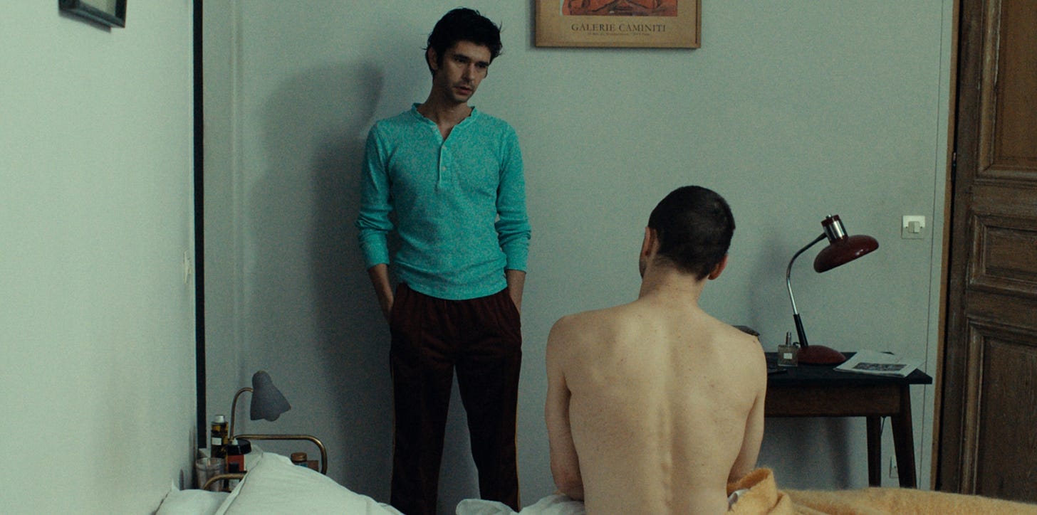 Clothed Ben Whishaw stands next to a nude, seated Franz Rogowski in "Passages" (2023)