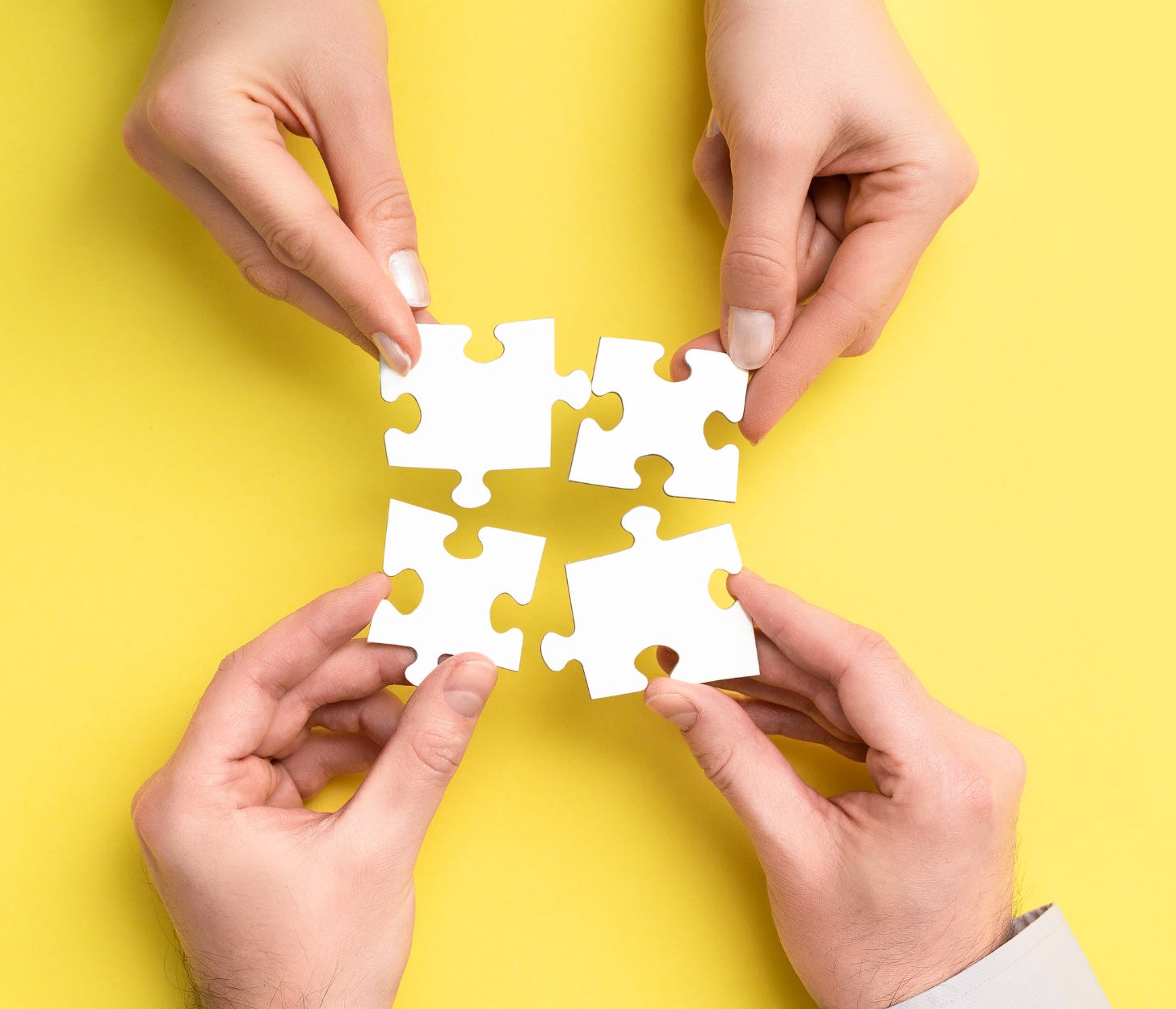 Two pairs of hands each hold two blank white jigsaw puzzle pieces against a yellow background.