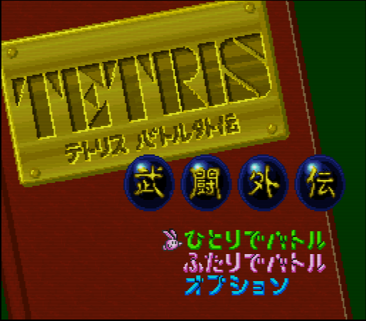 A screenshot of the title screen from the original Japanese release of Tetris Battle Gaiden, which shows the game's logo on the cover of a storybook, along with the various options for the single-player story mode, two-player battles, and options menu, all displayed in Japanese characters.
