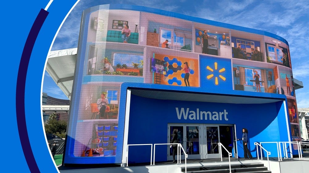 Booth of Walmart booth at Consumer Electronics Show in Las Vegas. Exterior shows multiple screens and woman standing at entrance of doors.