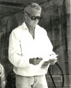 This may contain: an old black and white photo of a man in sunglasses looking at something on a paper