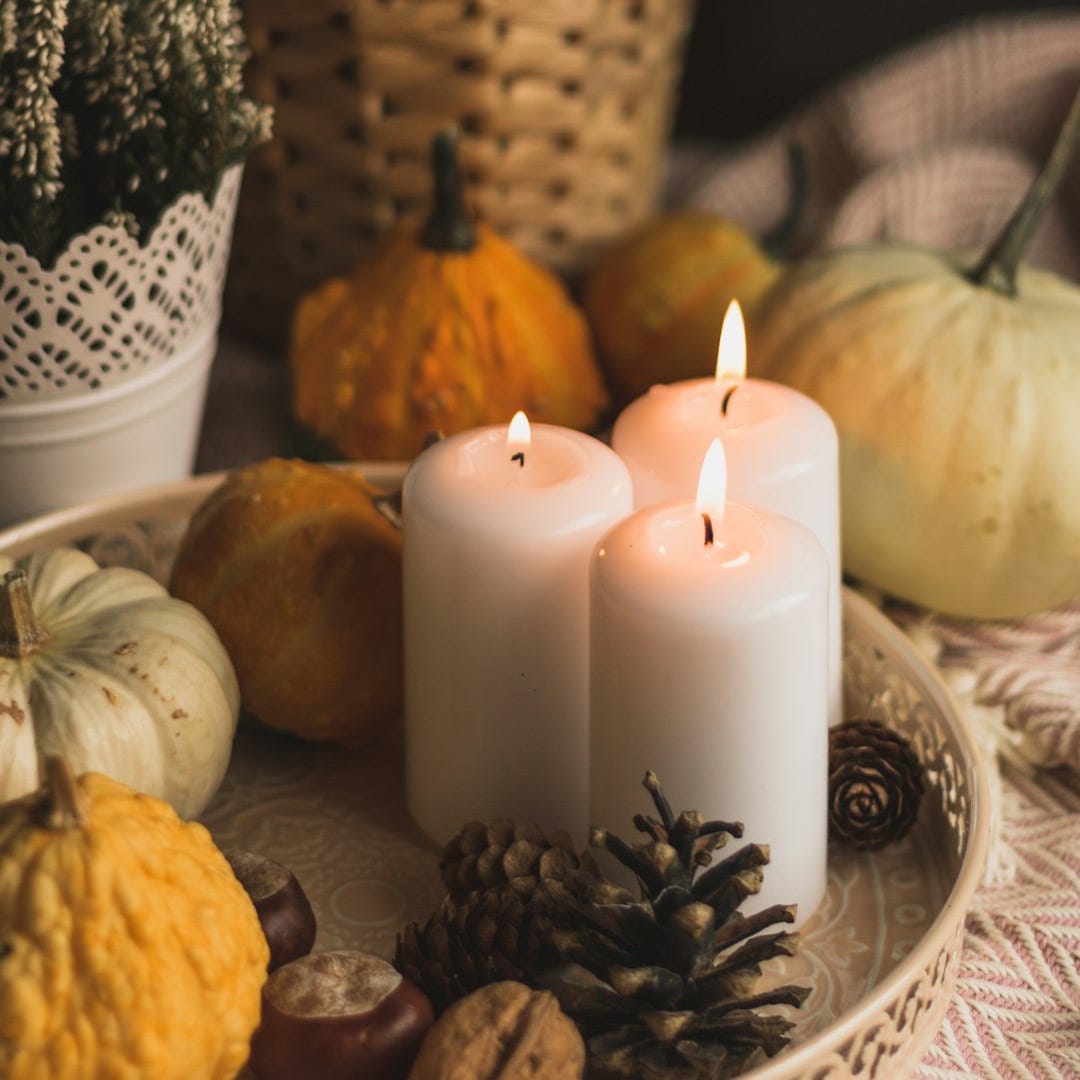 white pillar candle between orange pumpkins and white and black ceramic candle holder