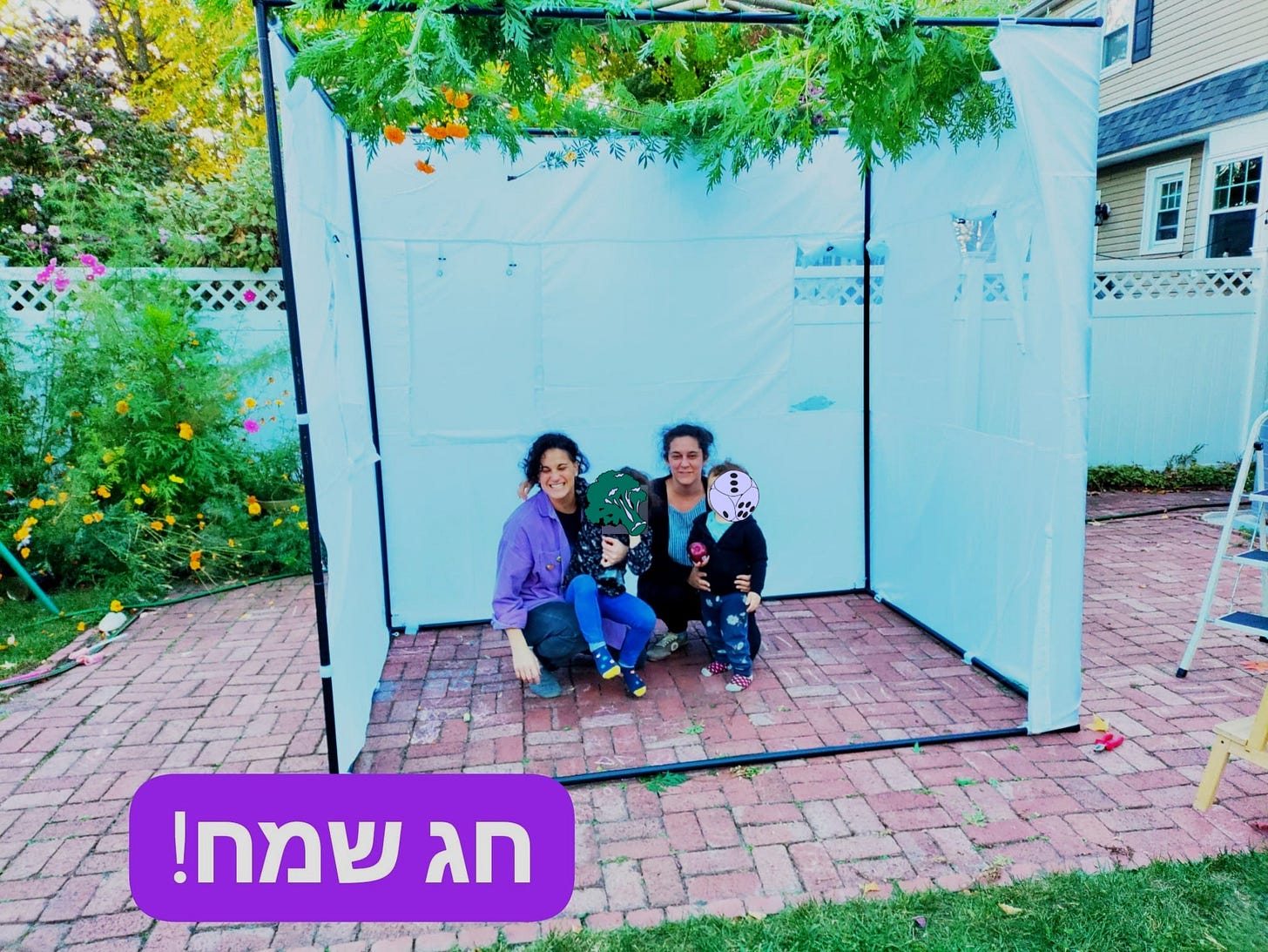 Mikhal, her wife, and two kids pose inside their little sukkah on a brickwork patio.