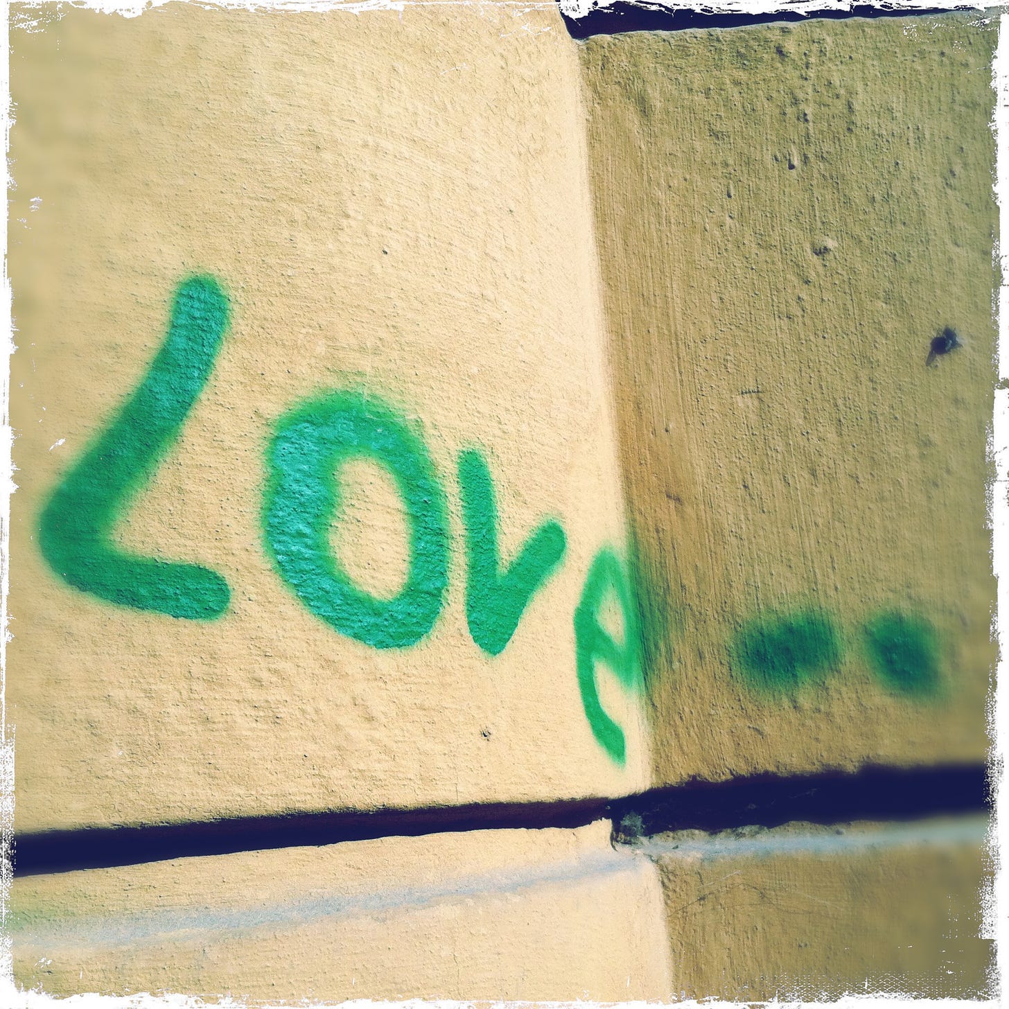 Green spray paint on yellow stone wall reading Love