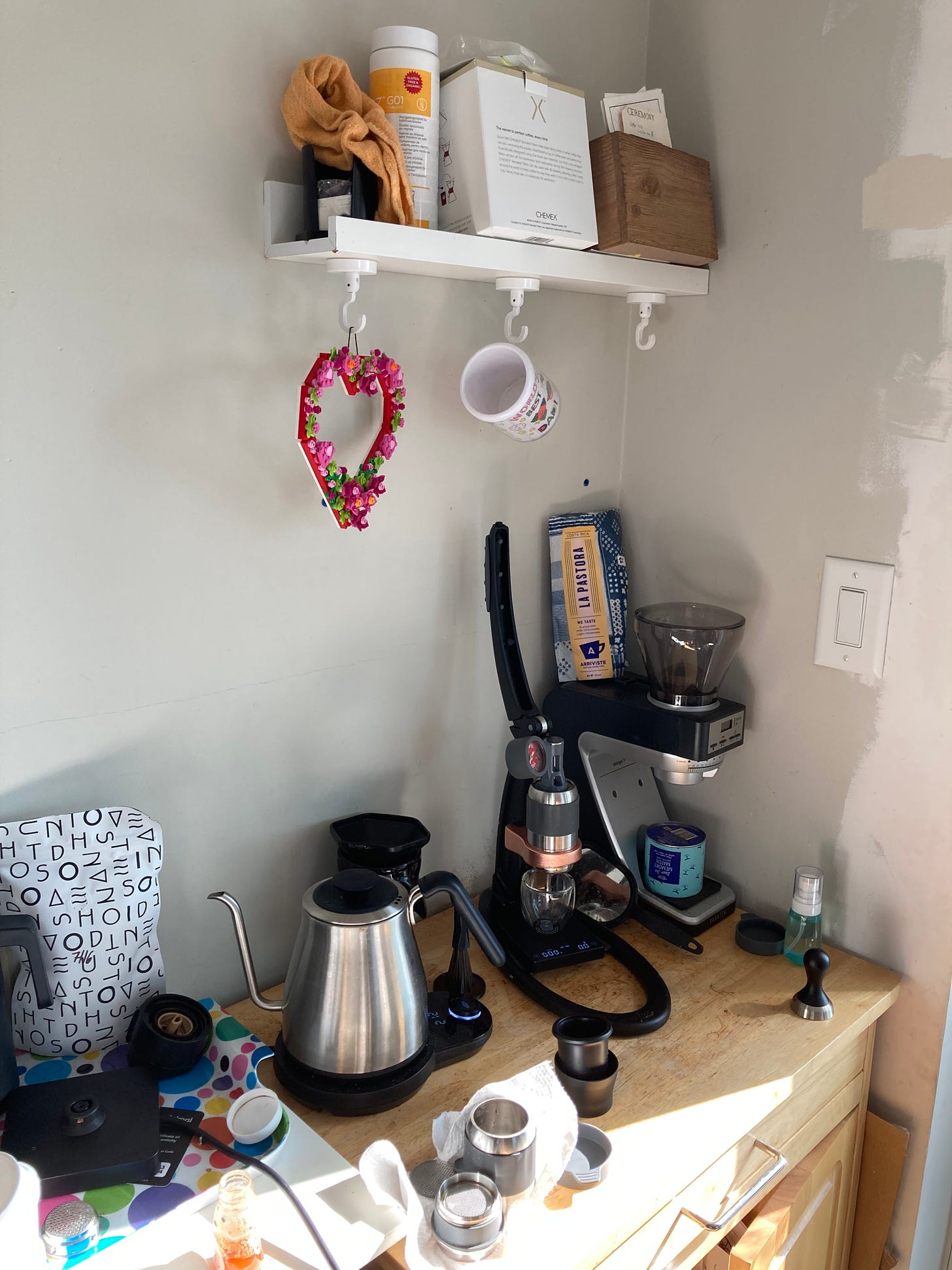 A coffee station with water hot pot, manual espresso machine, and coffee grinder as well as various coffee-making accessories.