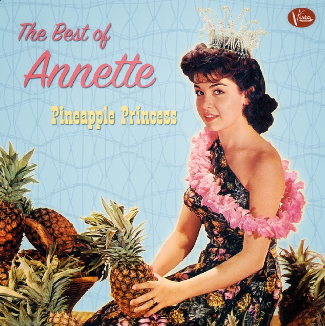 Annette Funicello in a pineapple print dress holding a pineapple, and wearing a sparkly white pineapple-inspired crown.