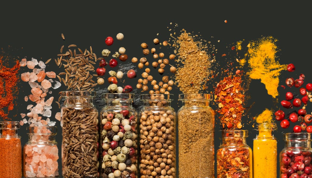 Assorted spices in transparent glass jars with some spices spilling out, set against a dark background.