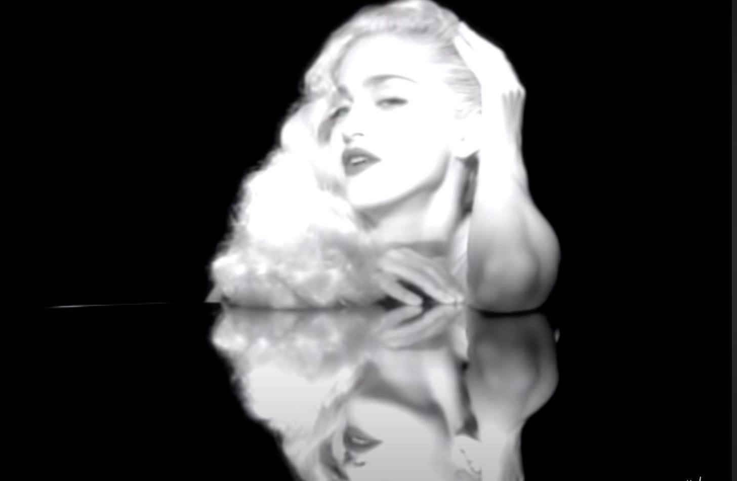 Madonna wears a long hair piece in the Vogue video as she sings over a reflective surface