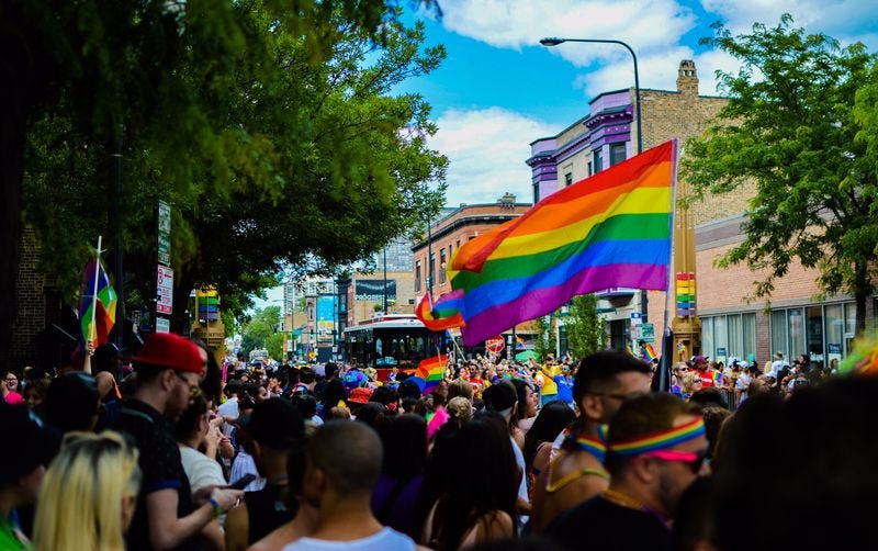 A pride parade on a city street in which many people are holding rainbow flags