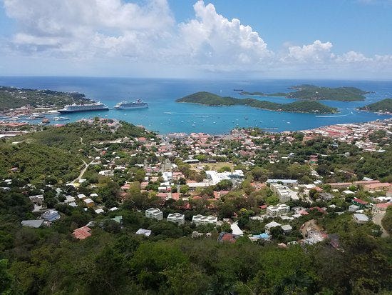 a view of charlotte amalie with a blue water harbour, trees surrounging the bay and open ocean in the background