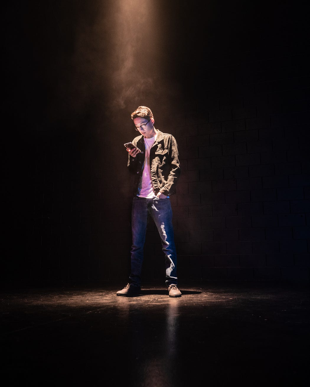 Young Asian man standing on a stage looking at his phone with a spotlight shining on him