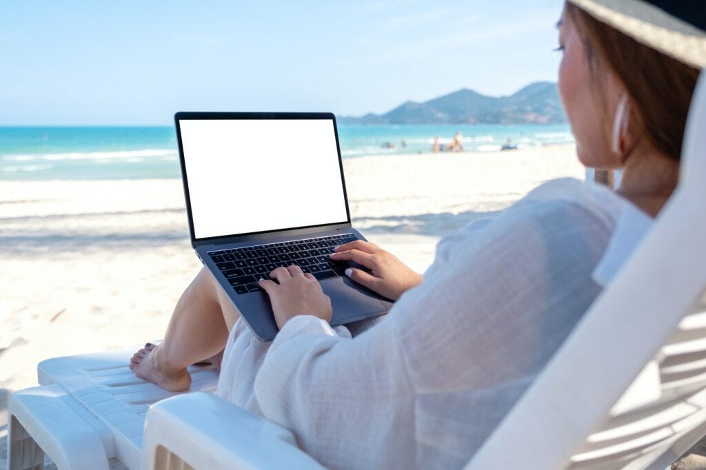 a woman using and typing on laptop computer with blank desktop screen on the beach