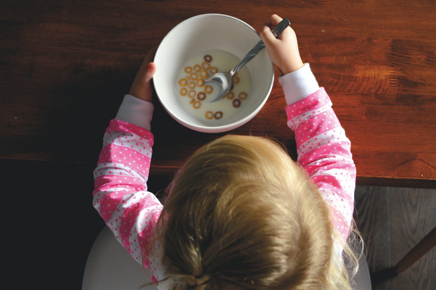 Child eating cereal from a white bowl on a table