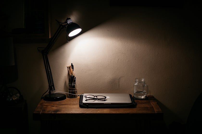 Lamp, laptop, and glasses on a wooden desk at night