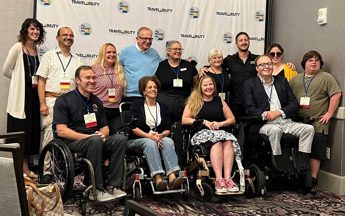 John photographed with a select group of summit attendees in front of a banner with the Travel Ability logo.