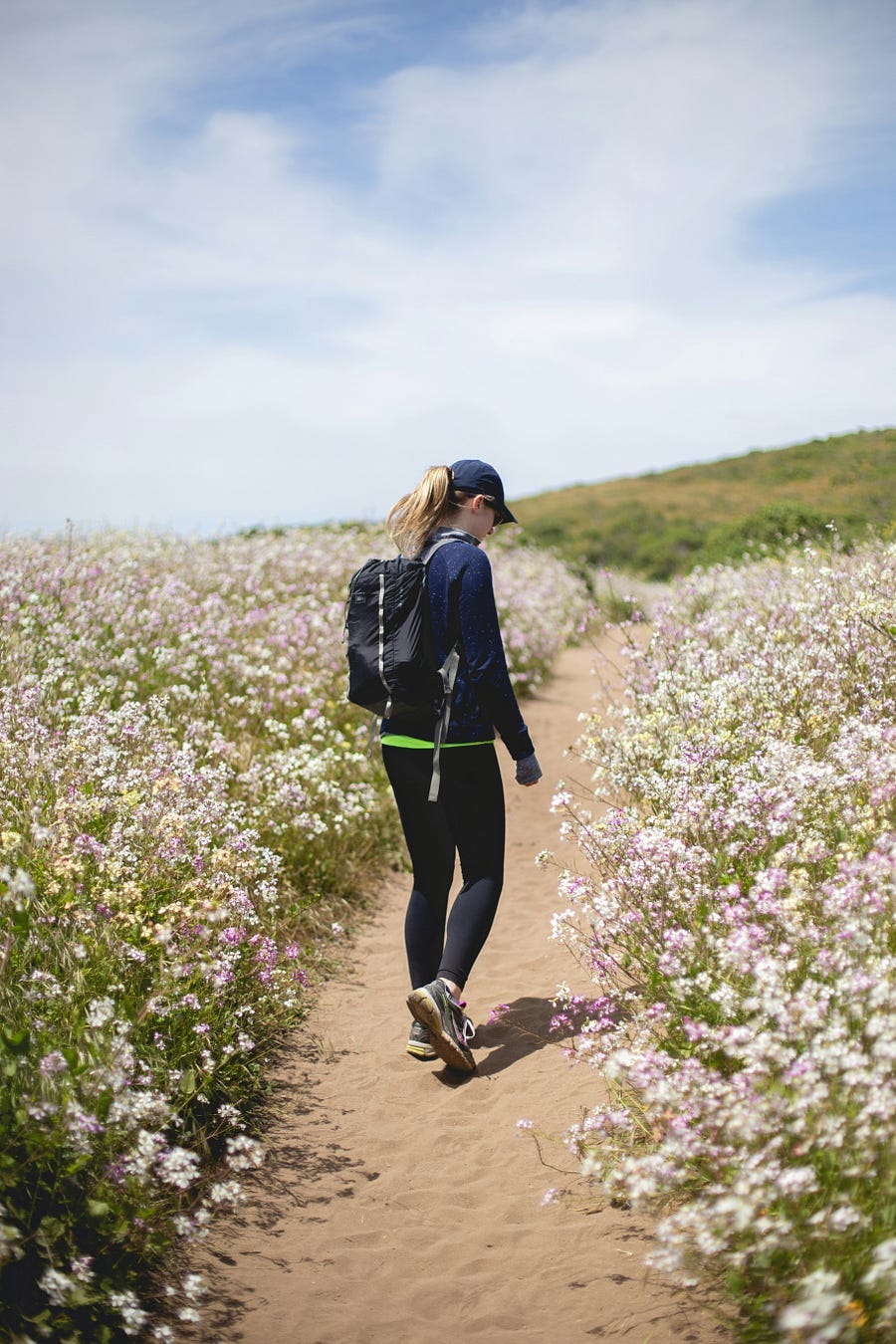 Woman walking a pathway through flowers on either side.