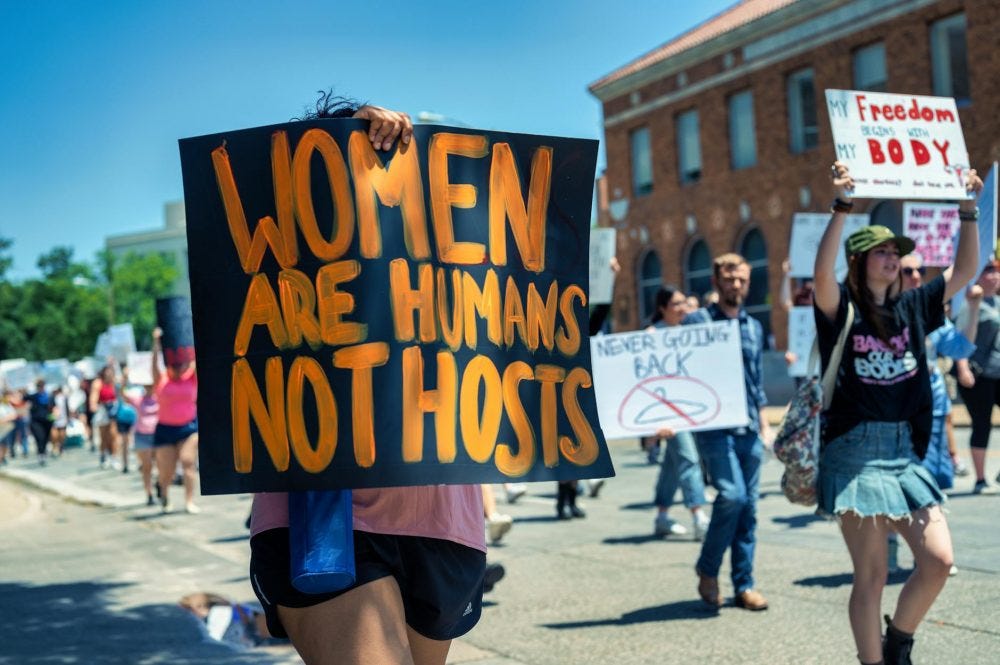 women walking on a street with banners at a protest about womens rights