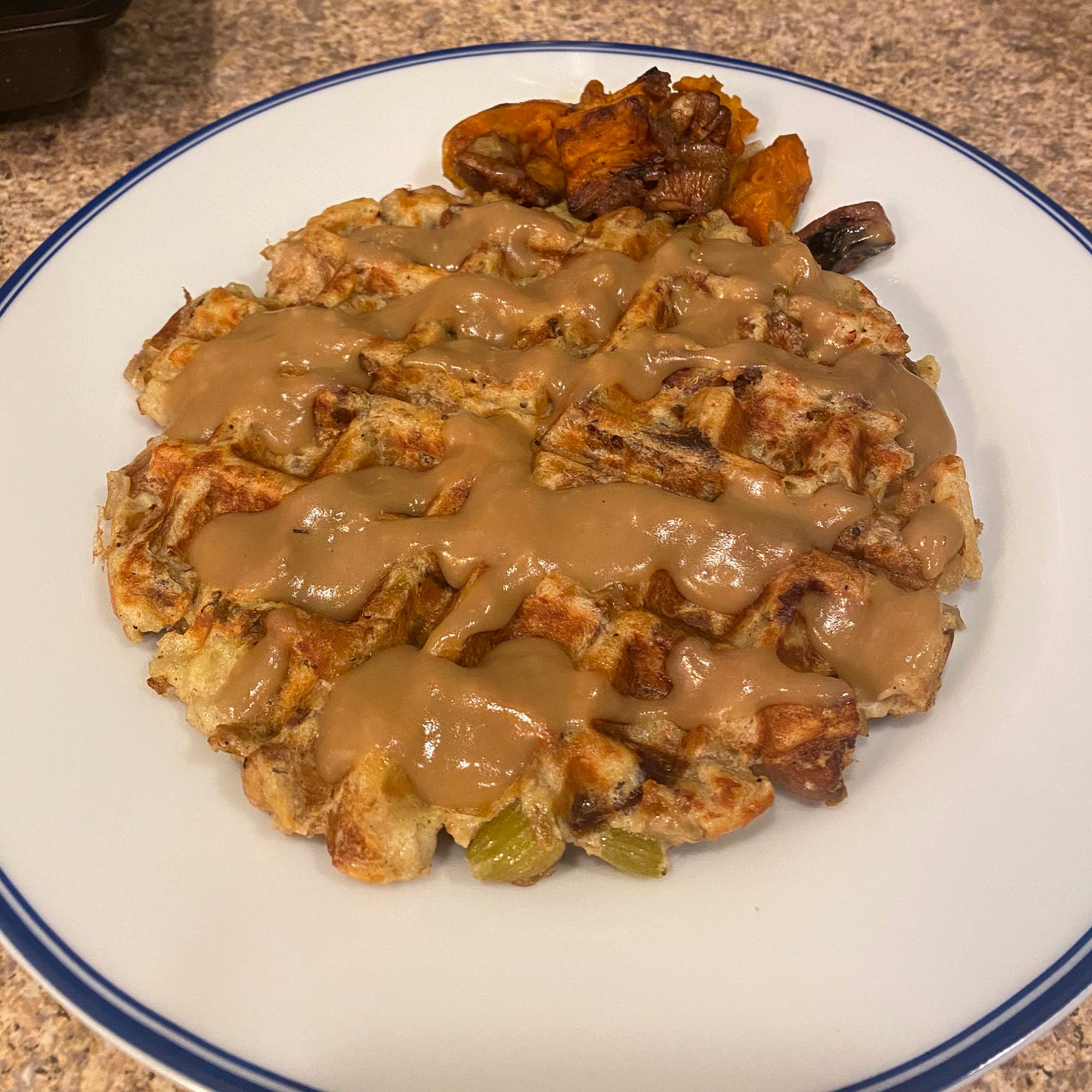A stuffing waffle with gravy overtop. A small amount of roasted yams & brussels sprouts sits to the side.