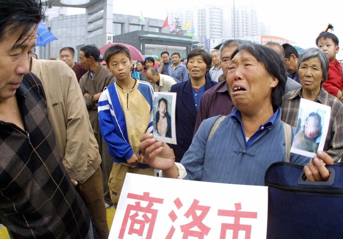  A peasant cries as she hold photos of her son who she alleged was brutalized and killed by the local officials, as she joins other petitioners queueing outside the new complaints bureau for their chance to submit their grievances in Xian, central China's Shaanxi province on Aug. 18, 2005. (STR/AFP via Getty Images)