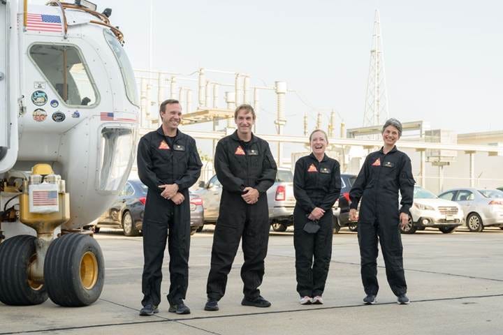 A group of people in black overalls standing in front of a helicopter

Description automatically generated
