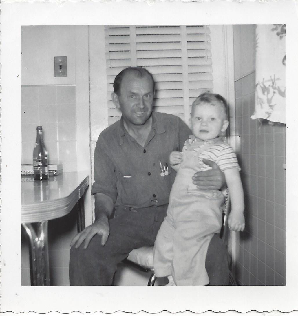 1950s era man sitting in his kitchen in his workclothes with his nephew on his knee