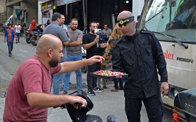 A member of the Al-Quds Brigades distributes candies in celebration of the deadly Hamas terror assault on Israel, at Lebanon's Beddawi refugee camp in Tripoli, Lebanon on October 7, 2023. (Fathi Al-Masri/AFP)