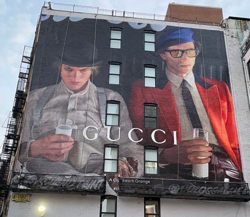 The same building with a mural of two men from Clockwork orange holding glasses of milk. The word GUCCI is centered.
