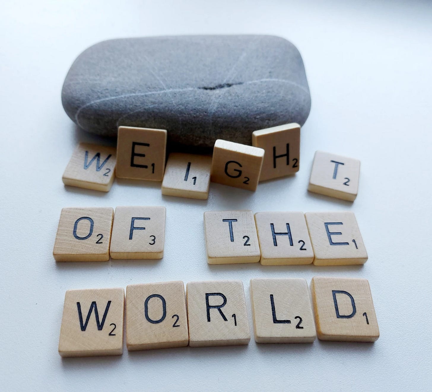 Scrabble letters forming the words ‘weight of the world’ and a grey stone crushing the top row