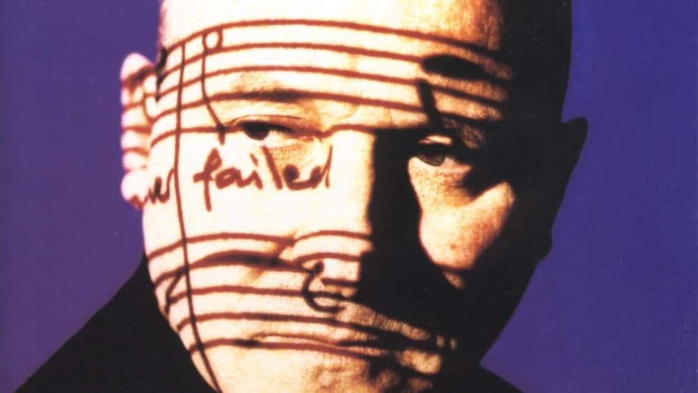 A photo of Gavin Bryars against a purple backdrop with lyrics and musical notation projected onto his face