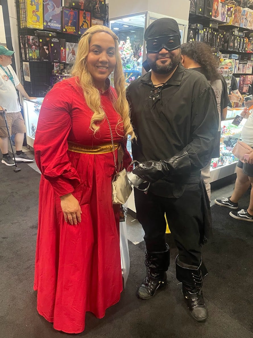 Couple dressed in a flowy red dress and blonde wig and a black pirate outfit with black mask and sword