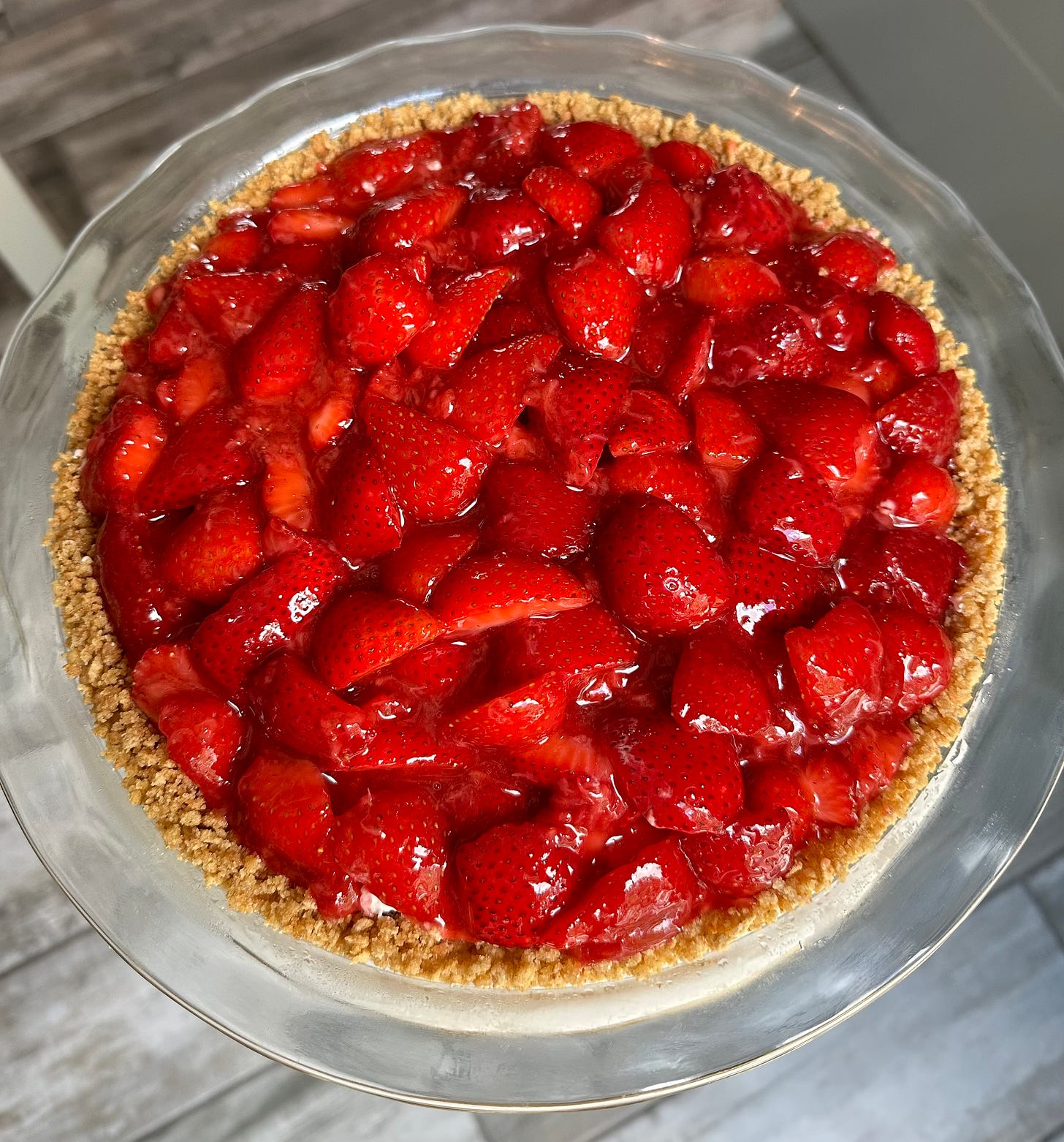 A glass pie pan shot from above filled with a golden graham cracker crust and tons of beautiful glazed strawberries