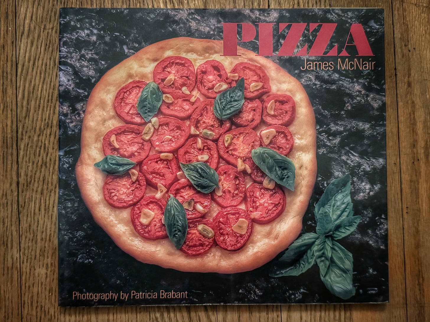 The cover of Pizza by James McNair, showing a very dry-looking pizza crust topped with slices of tomato and garlic as well as basil leaves. It's very 1990s.