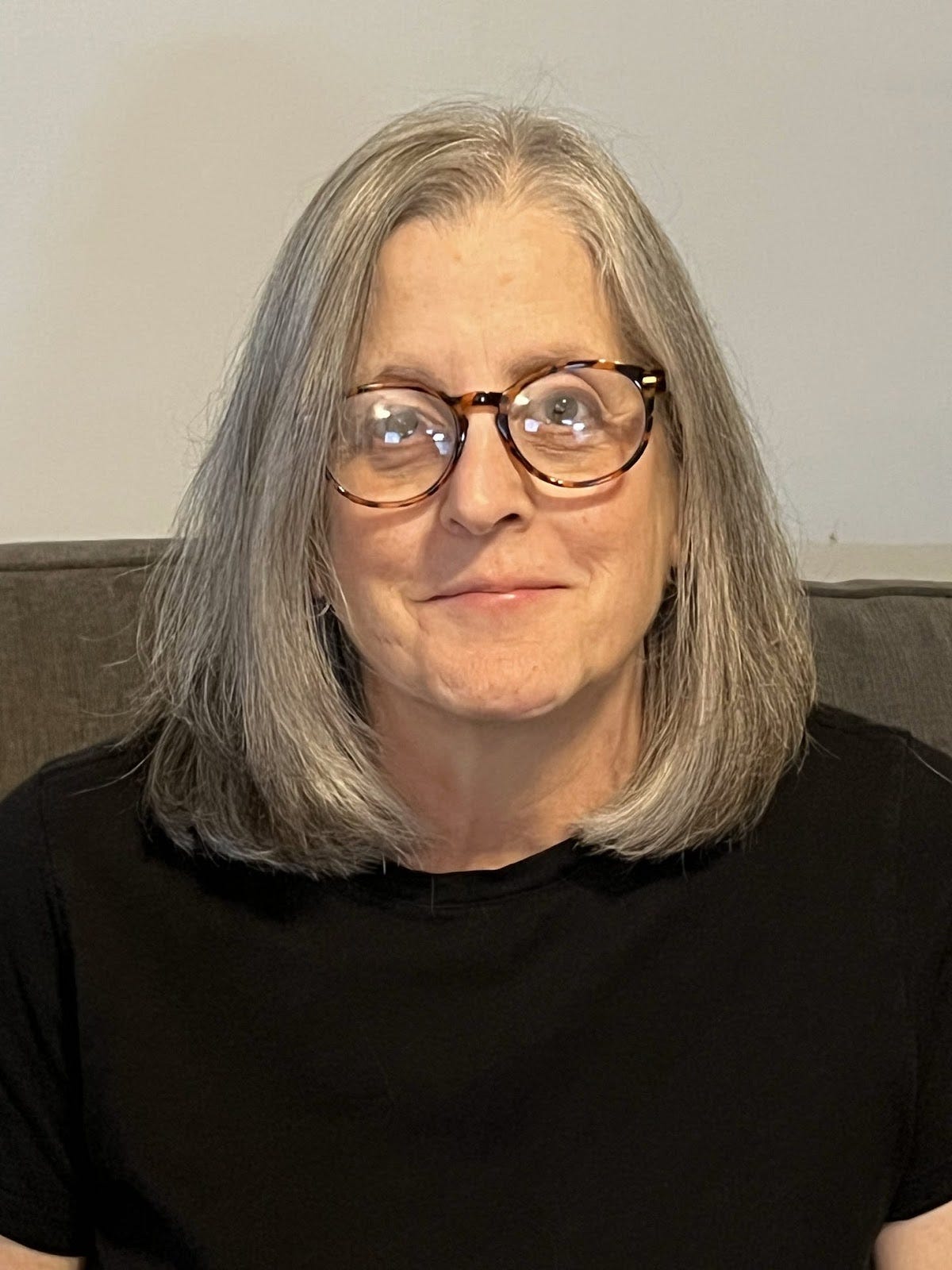 Jo Raphael is a white woman with gray shoulder length hair and glasses