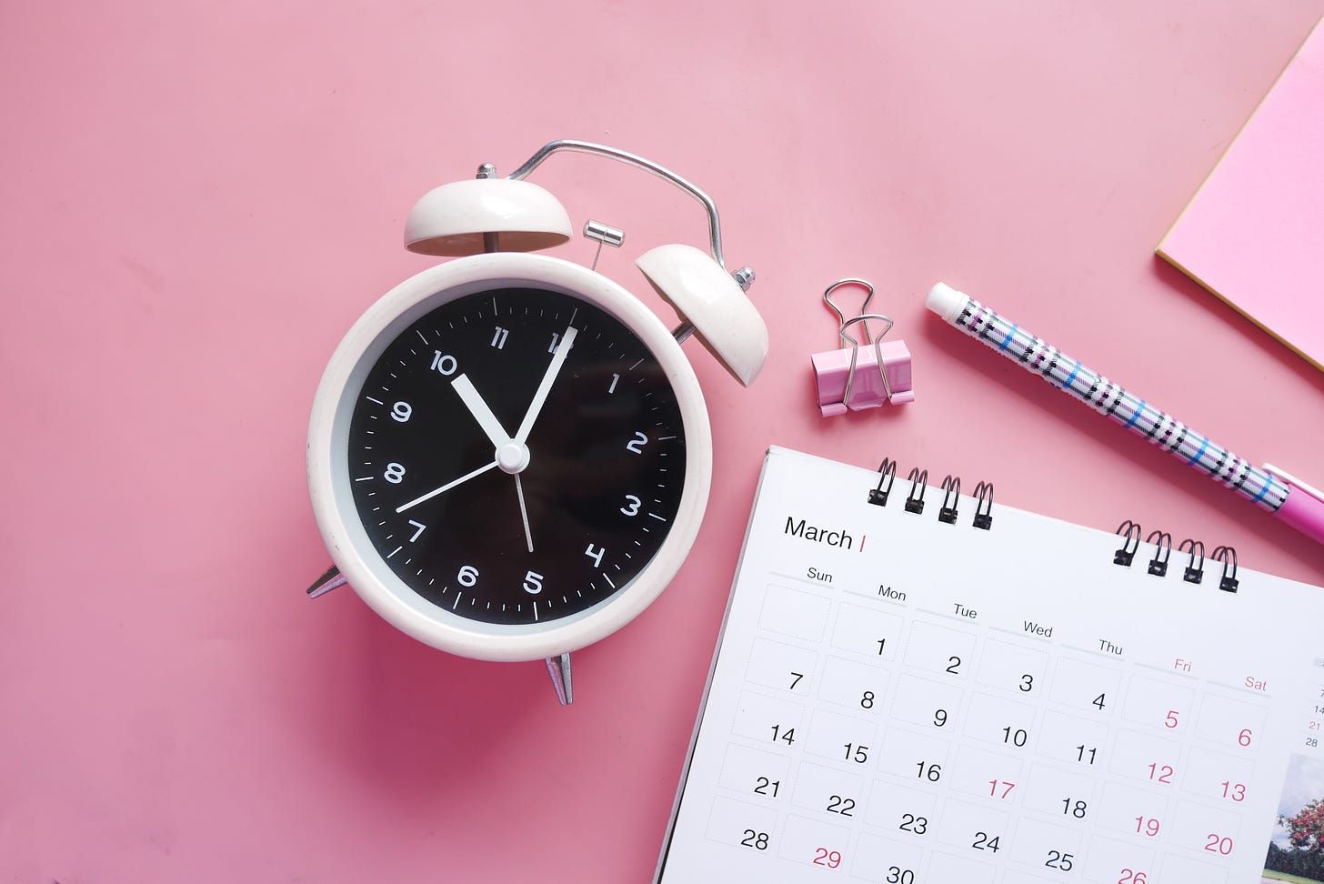 clock and notebook and pencil on pink background