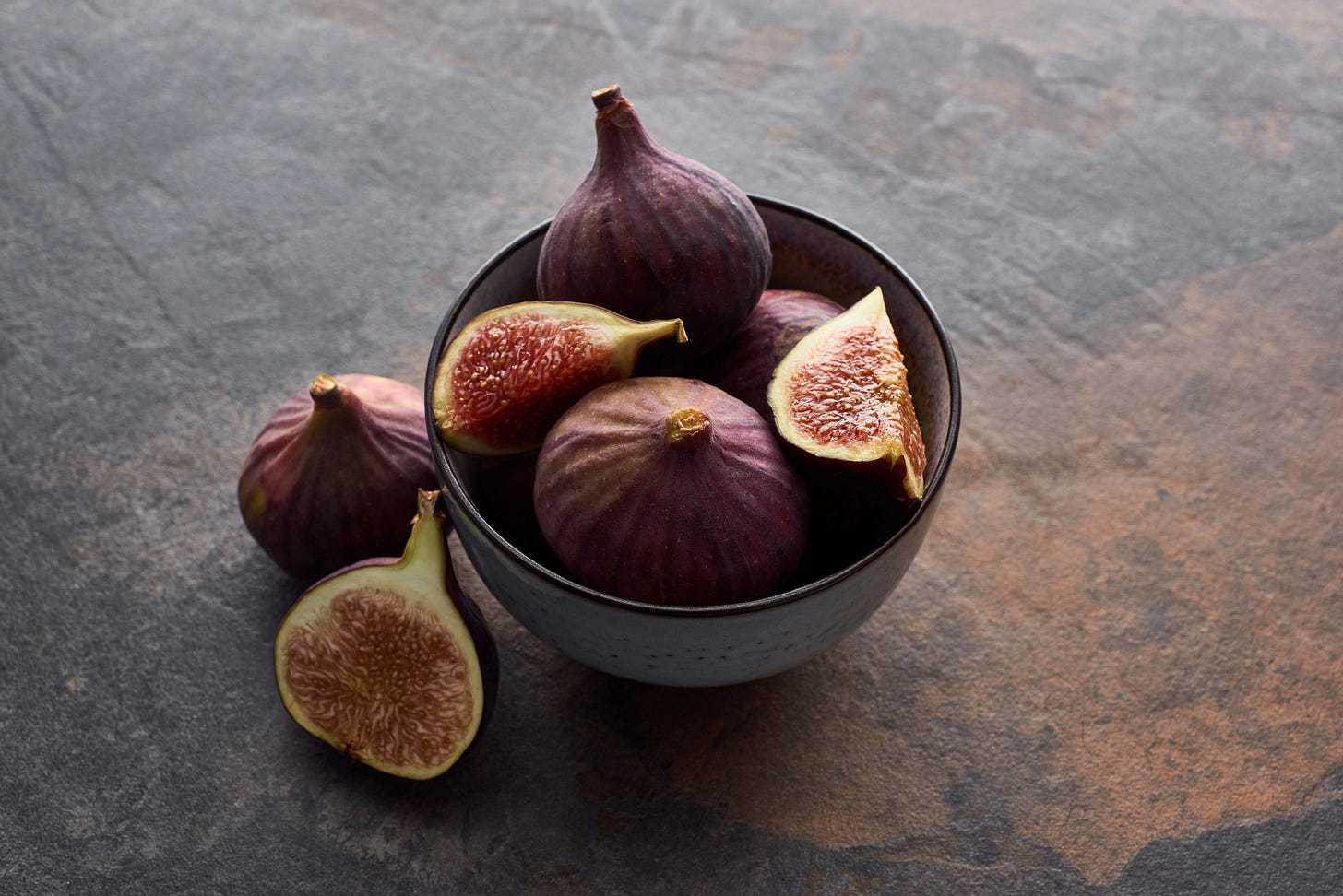 A bowl of ripe figs, some cut open, on a slate table