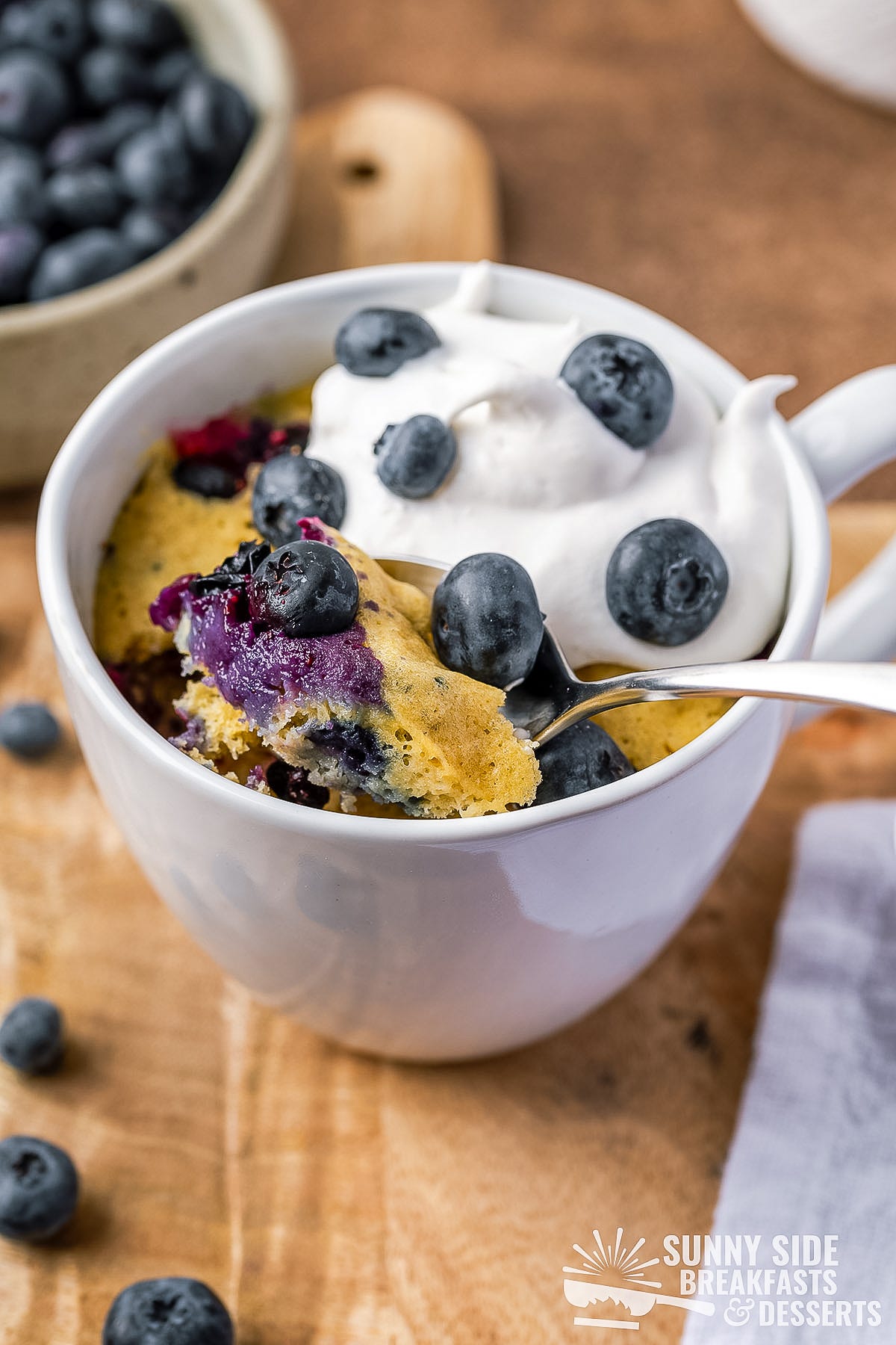 Spoon taking a scoop of blueberry muffin in a mug.