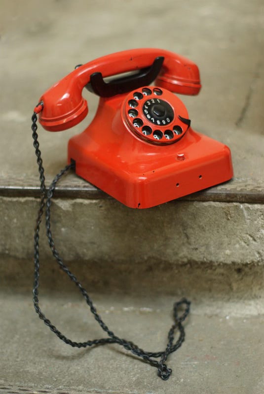 A candy red phone sits on a concrete step. What secrets were whispered on that line?