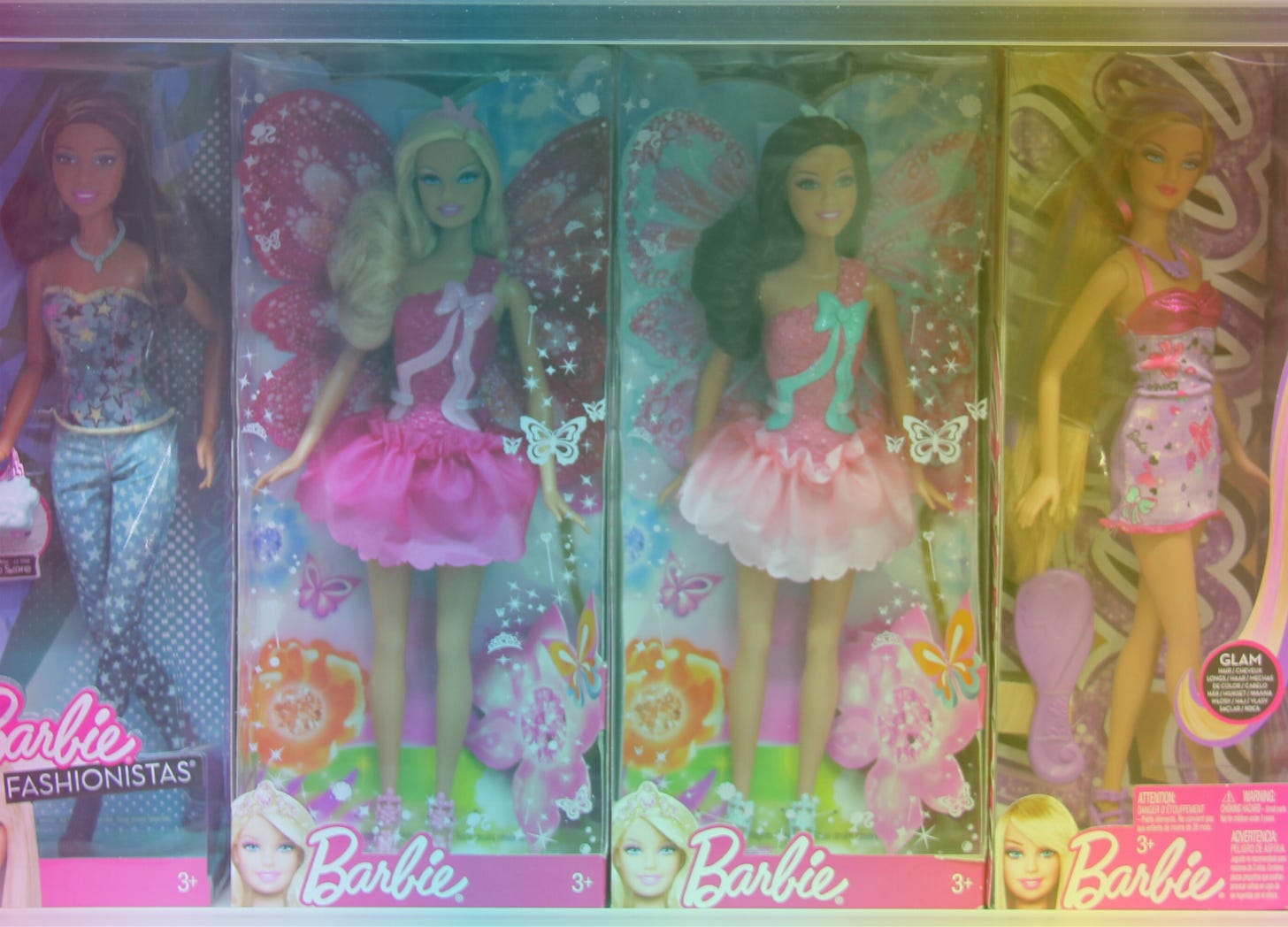 A rainbow-filtered photo of four different Barbies in their plastic boxes lined up next to each other on a toy store shelf