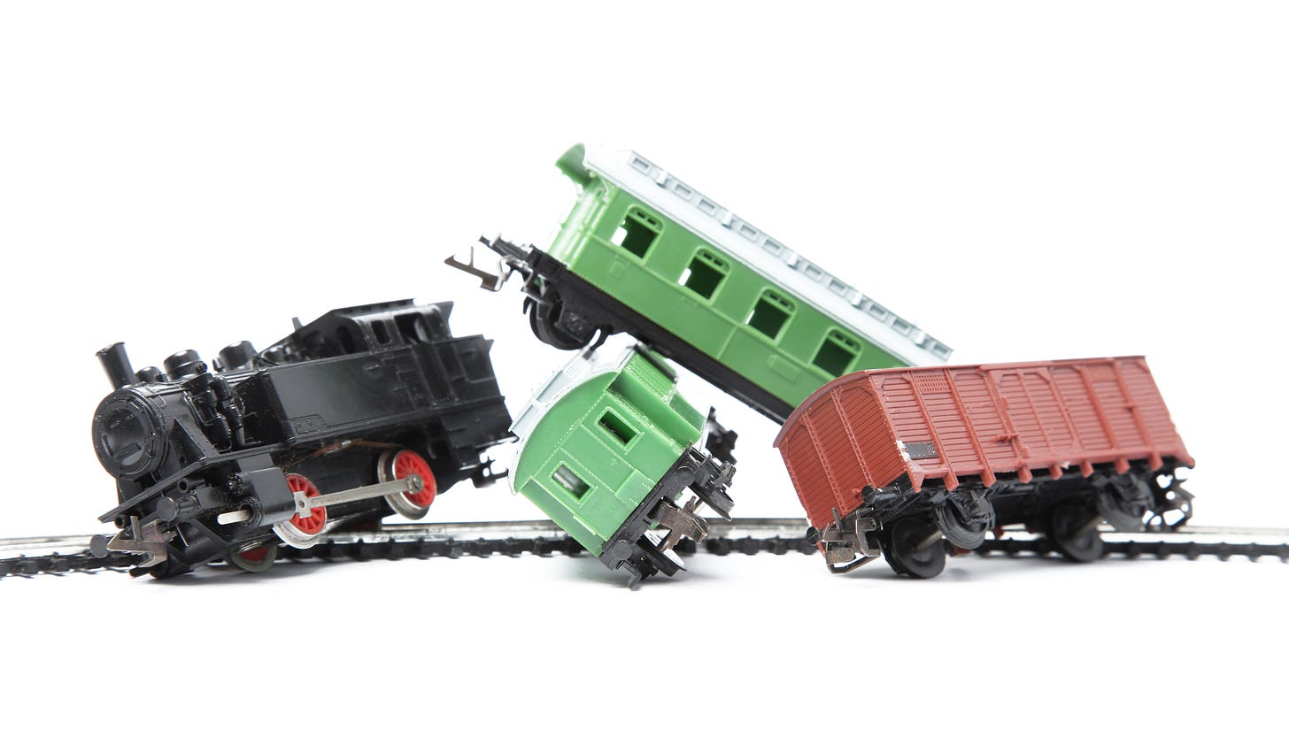 toy trains, a black engine, two green cars, and a red car piling up on a toy track to simulate a train wreck